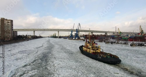 Flying over cargo port. The tugboat moving through an ice. Aerial drone footage
