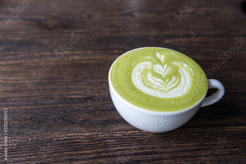 Hot green tea matcha latte in a cup on wooden table, top view