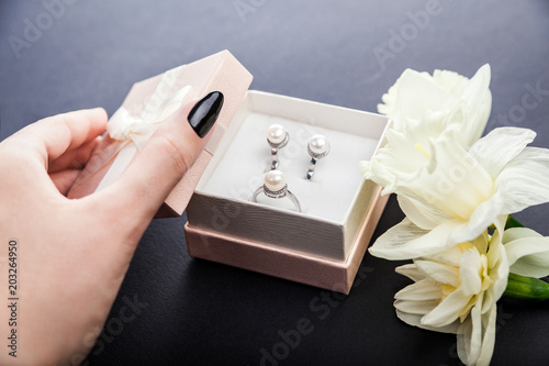 Woman opens gift box with pearl jewellery. Set of earrings and ring with flowers as a present for Mother's day.