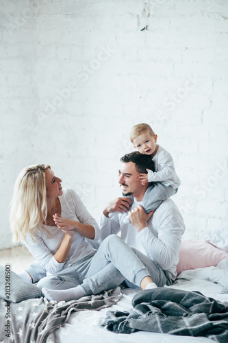 Young family playing and have fun sits on the bed. Mother, father and child. Indoor