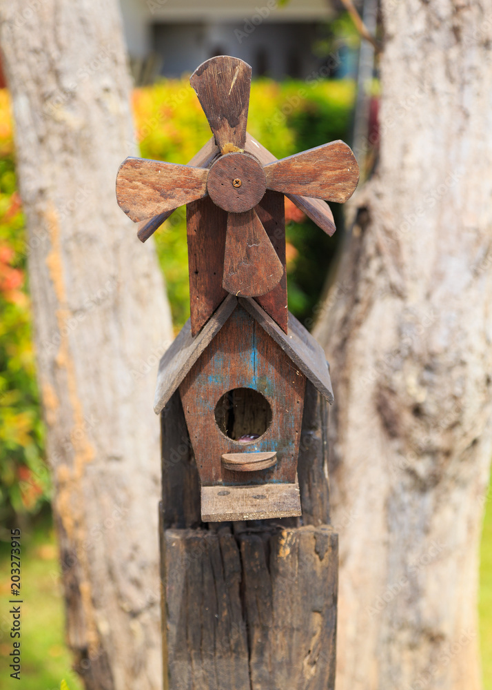 Closeup of bird wood house with gable roof and windmill in the garden Closeup of bird wood house with gable roof and windmill in the garden