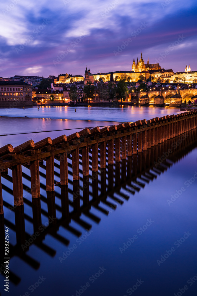 Beleuchtete Karlsbrücke und Prager Burg bei Dämmerung mit Damm der Moldau