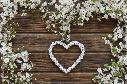 Close-up photo of Beautiful white Flowering Cherry Tree branches with white heart shape. Wedding  engagement or betrothal concept on vintage wooden background. Top view  greating card.