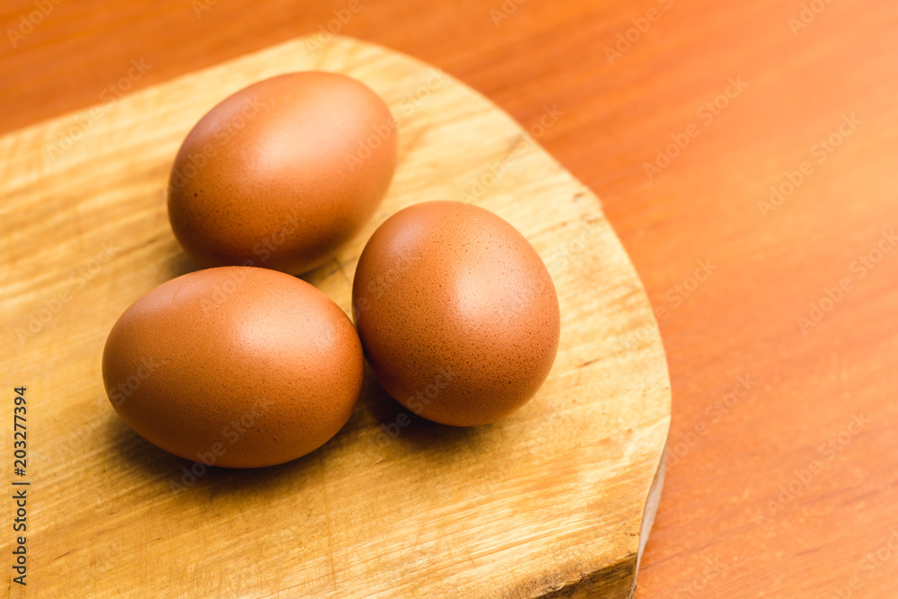 Three brown chicken eggs on a wooden cutting board