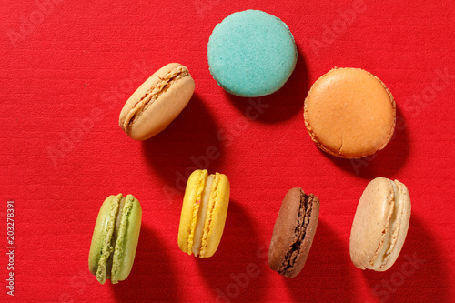 Sweet macarons cakes of different color on red textured surface