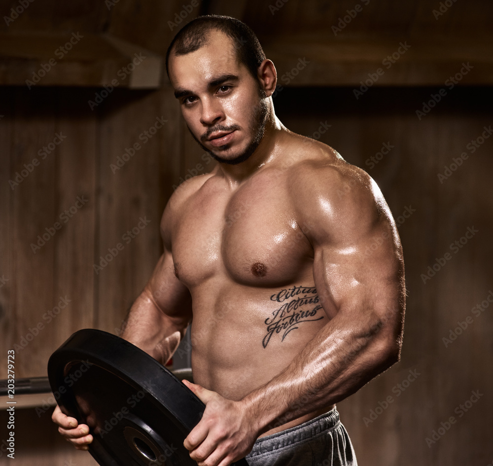 Portrait of handsome muscular athlete holding plate for weightlifting