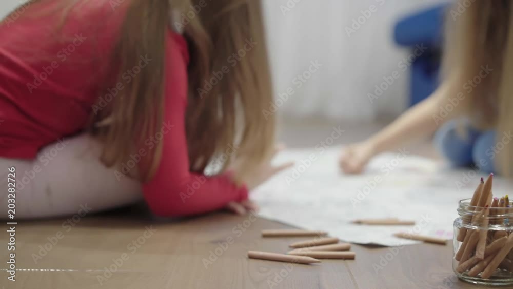 Hands of unrecognizable little girls drawing a large picture on the floor with pencils. Left to right pan real time establishing shot Hands of unrecognizable little girls drawing a large picture on the floor with pencils. Left to right pan real time establishing shot