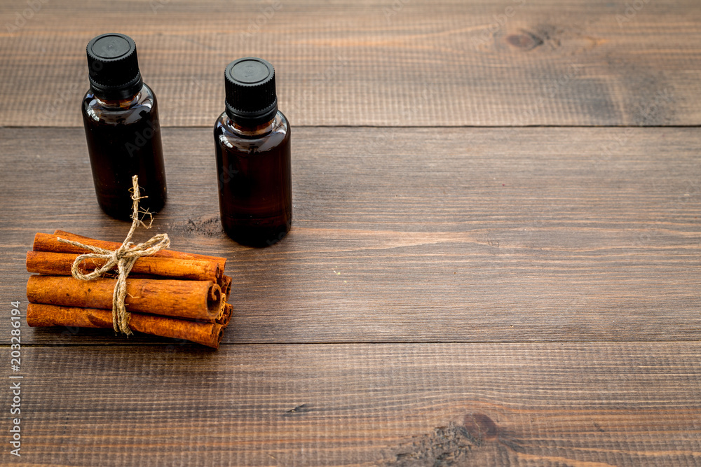 Cinnamon oil for cooking, aromatheraphy, skin care. Bottles near cinnamon sticks on dark wooden background space for text