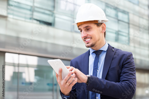 Male architect in helmet working at the tablet