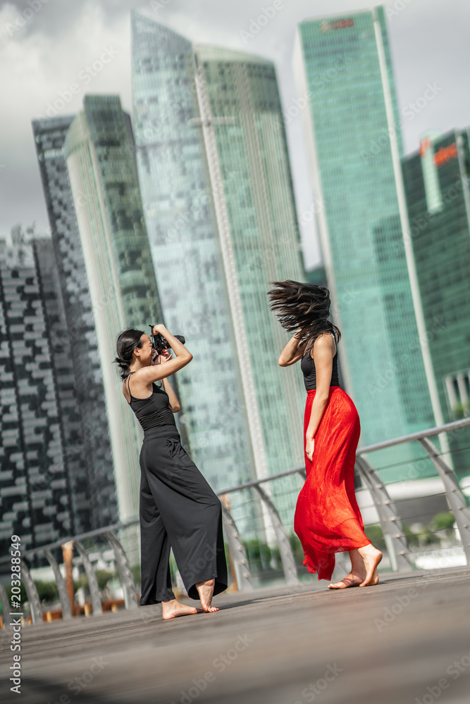 Two beautiful young girls having fun photo shooting on a deck with skyscrapers city background