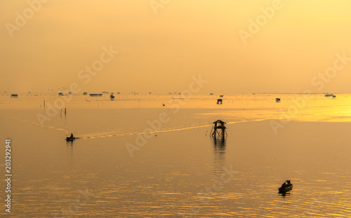 Silhouette of fisherman with his boat in the sea during sunrise. © Success Media