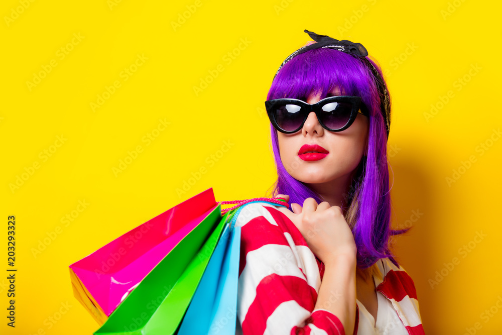 Young girl with purple hair holding shopping bags on yellow background. Consumer concept Young girl with purple hair holding shopping bags on yellow background. Consumer concept