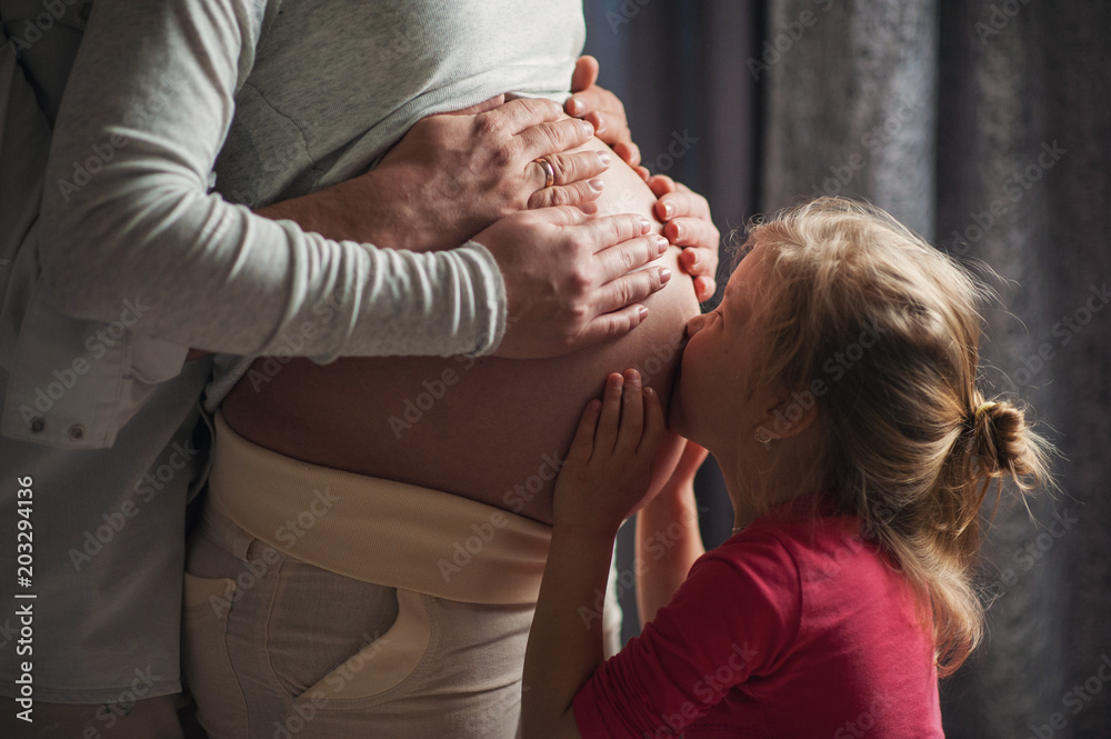 A little girl kisses the belly of her pregnant mother. Mom expects the birth of a girl A little girl kisses the belly of her pregnant mother. Mom expects the birth of a girl