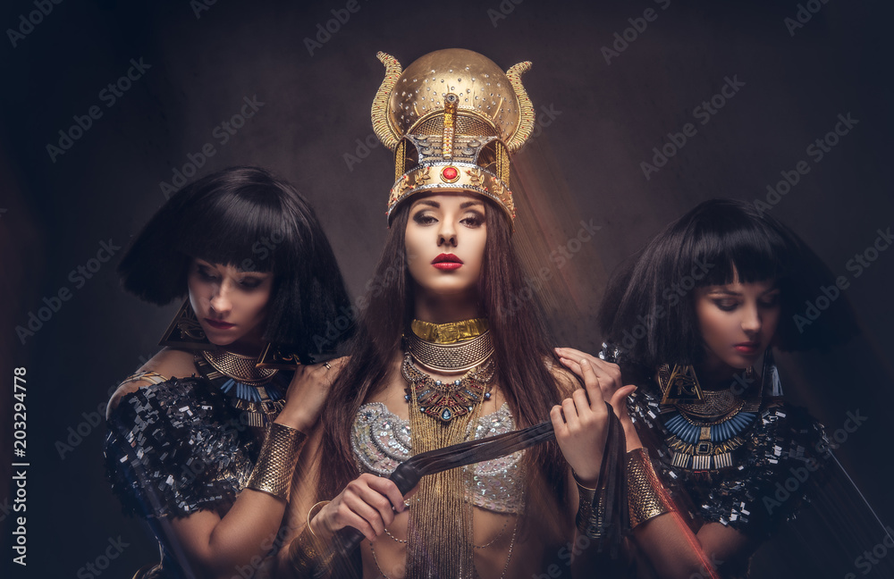 Fototapeta premium Portrait of haughty Egyptian queen in an ancient pharaoh costume with two concubines.