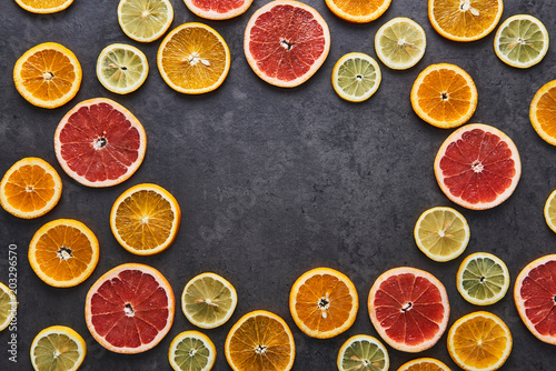 Fototapeta Naklejka Na Ścianę i Meble -  Flat lay of citrus fruits circular pattern of lemon, orange and grapefruit on black stone background. Copy space in the middle. Top view.