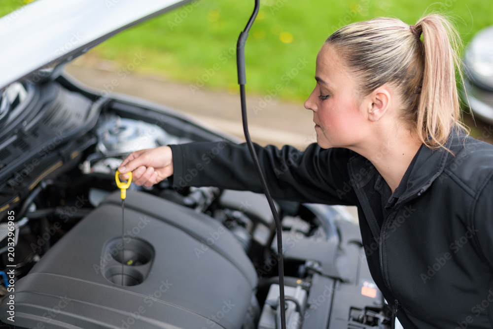 A woman mechanic checking a car's oil level at roadside