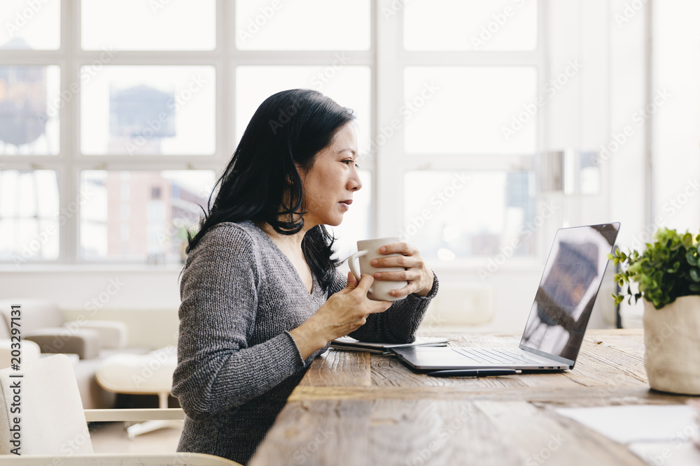 Businesswoman holding coffee cup while using laptop in office Businesswoman holding coffee cup while using laptop in office