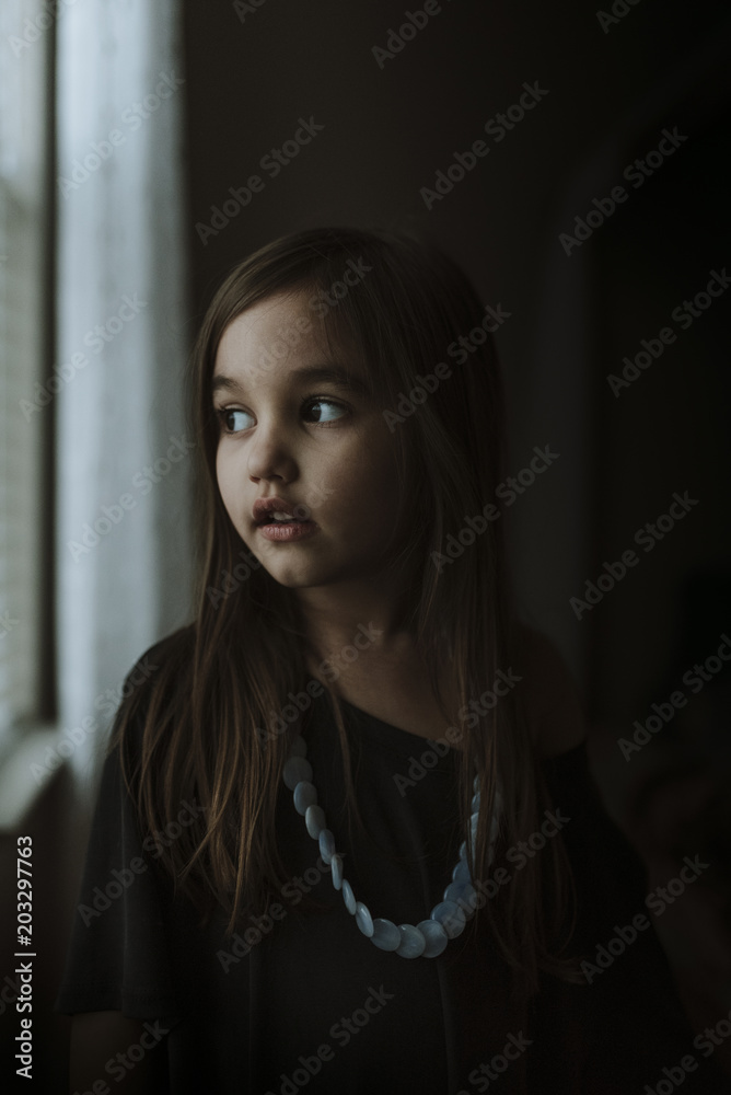 Close-up of thoughtful girl looking through window while standing in darkroom at home