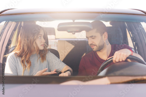 Nervous female indicates at watch, shows it husband, warns that they are late for meeting, stand in traffic jam while drive in car. Family couple hurry for birthday party, pose in automobile © sementsova321