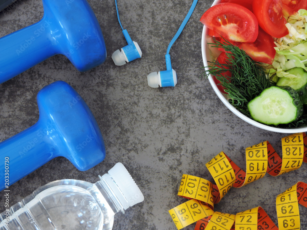 Dumbbells, measuring tape, water, telephone with headphones, bowl with salad. The concept of fitness, healthy eating and active lifestyle.