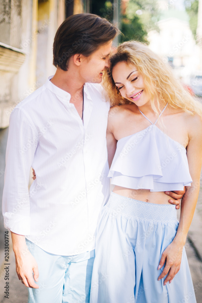Naklejka premium Happy newlywed couple on a relaxing walk in sunny Paris during summer honeymoon, smiling man hugging beautiful woman in hipster blue top and skirt outdoors