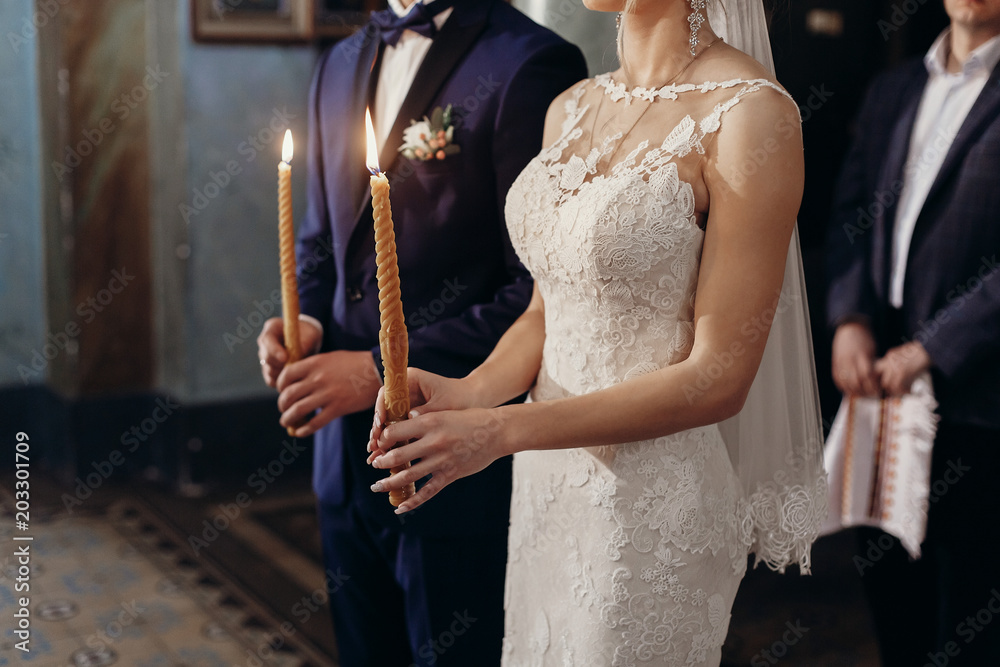 Beautiful bride and groom holding candles during wedding ceremony in church, gorgeous blonde bride and handsome groom performing spiritual ritual, marriage concept
