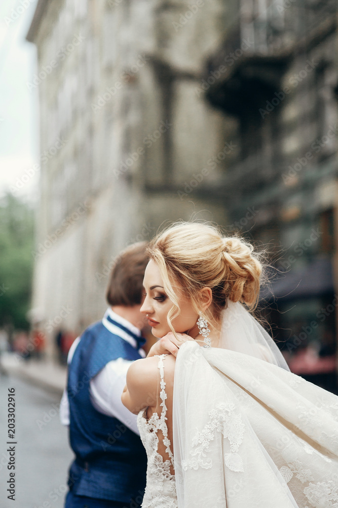 Stylish bride in white wedding dress with veil walking on street, back shot with naked spine, elegant bride concept