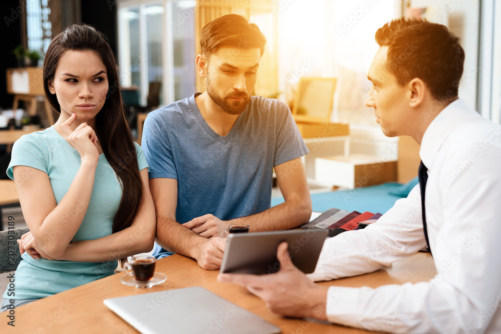 The manager of the furniture store is showing to the guy and the girl examples of furniture design on tablet. The manager of the furniture store is showing to the guy and the girl examples of furniture design on tablet.