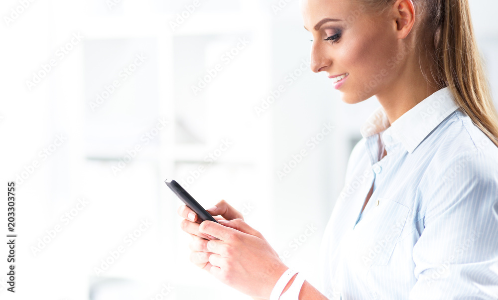 Businesswoman sending message with smartphone sitting in the office Businesswoman sending message with smartphone sitting in the office