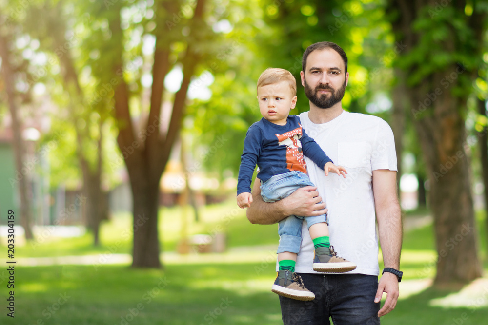 Father holding his toddler son outdoors in park on sunny spring day. Natural lighting, no retouch, closeup, vibrant colors Father holding his toddler son outdoors in park on sunny spring day. Natural lighting, no retouch, closeup, vibrant colors