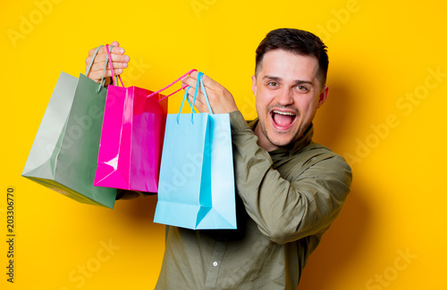 Young happy man with colorful shopping bags on yellow background