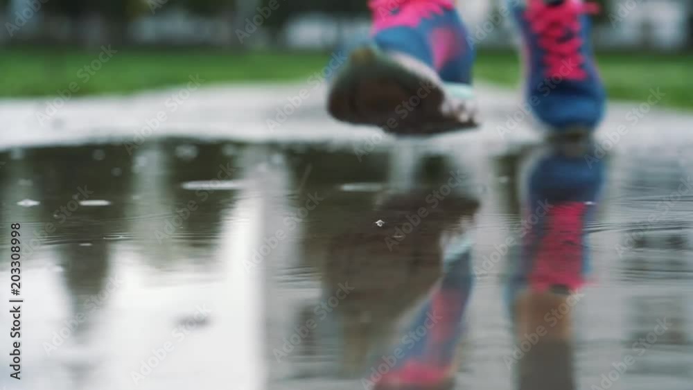 Close up shot of legs of a runner in sneakers. Female sports man jogging outdoors in a park, stepping into muddy puddle. Close up shot of legs of a runner in sneakers. Female sports man jogging outdoors in a park, stepping into muddy puddle.