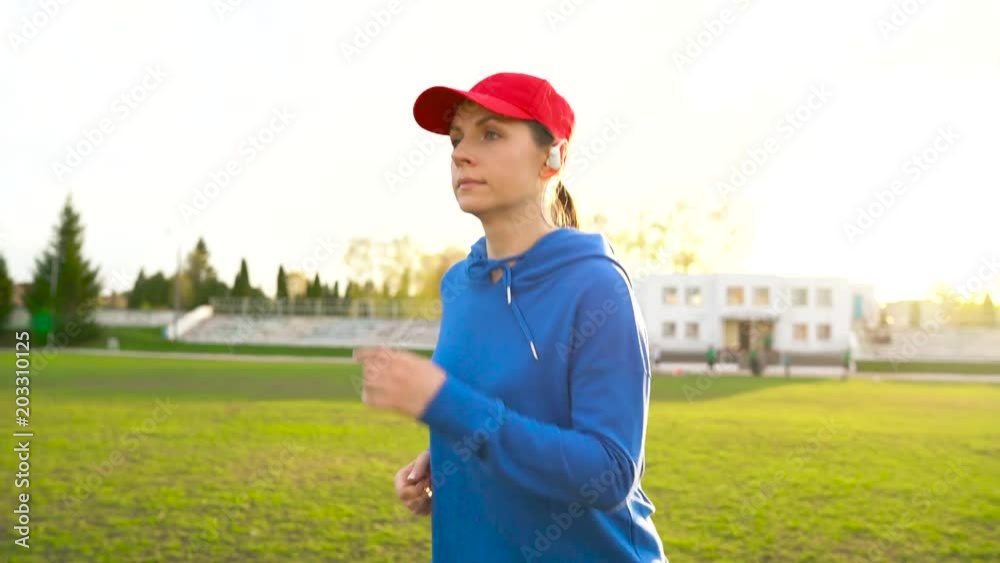 Woman with wireless headphones runs through the stadium at sunset Woman with wireless headphones runs through the stadium at sunset