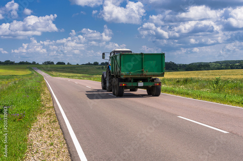 Tractor rides on the asphalt road in the sunlight