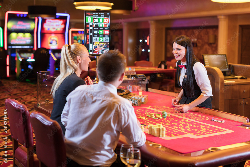 Cute lady casino dealer at Roulette table. Happy couple is playing Roulette. Cute lady casino dealer at Roulette table. Happy couple is playing Roulette.