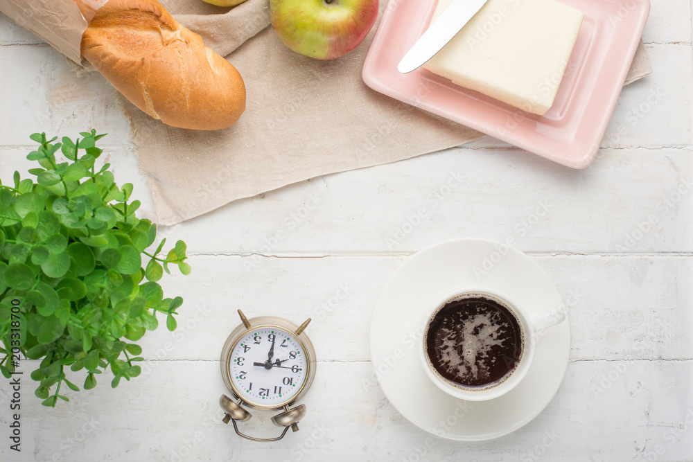 Morning cup of coffee, alarm clock, apples, butter and baguette, in a light kitchen. Background area, the concept of a bright morning and breakfast. Top view, with empty space for inscription