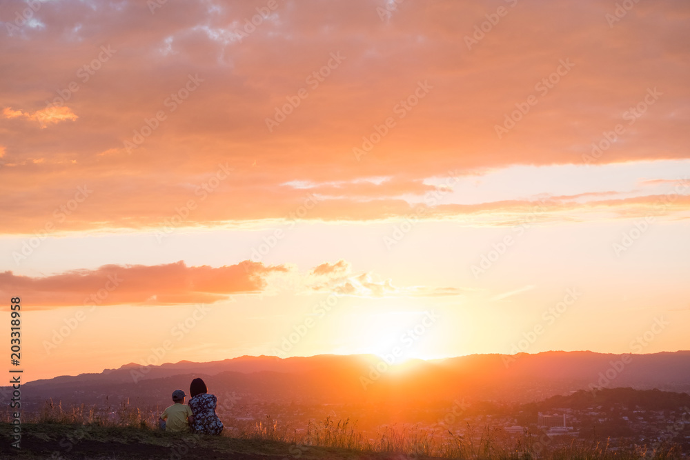 Obraz premium Mom and son enjoy together their sunset over the mountain and the town.