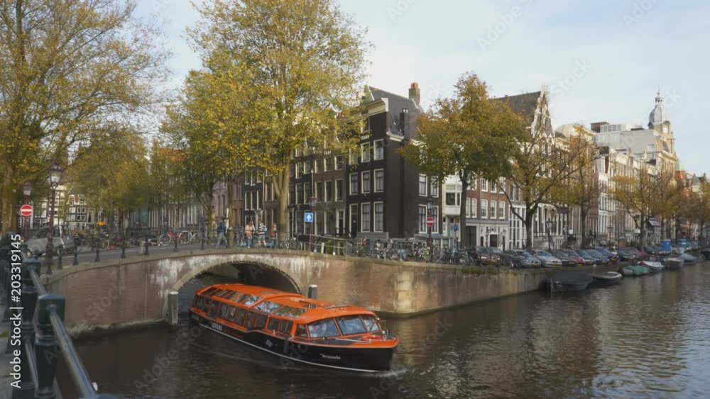 an orange tour boat passes under a canal bridge in amsterdam, netherlands
