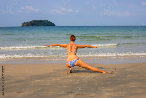 Woman doing yoga on empty beach. Tropical seaside vacation activity. Young girl in asana posture.