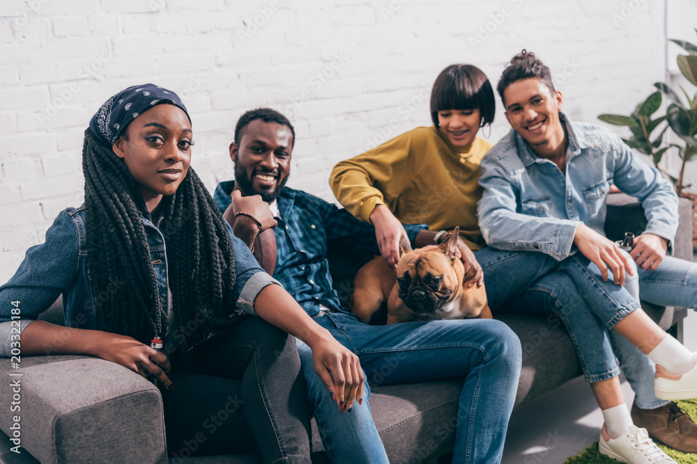 group of young multiethnic friends sitting on couch with dog