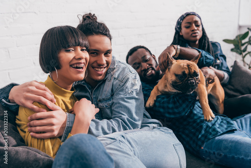 young smiling group of multicultural friends sitting on couch with dog