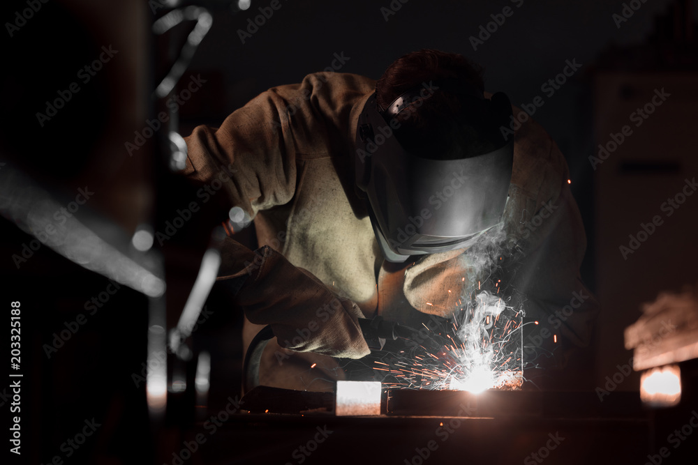front view of welder in protection mask working with metal at factory front view of welder in protection mask working with metal at factory