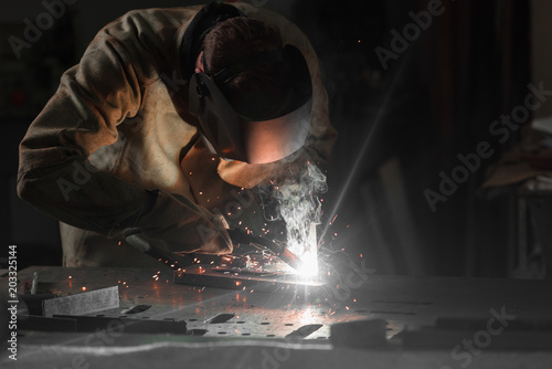 worker in protection mask welding metal at factory