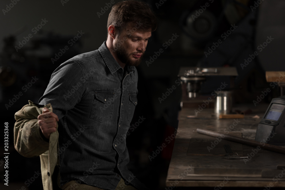 young male worker taking off uniform and sitting near table at factory young male worker taking off uniform and sitting near table at factory