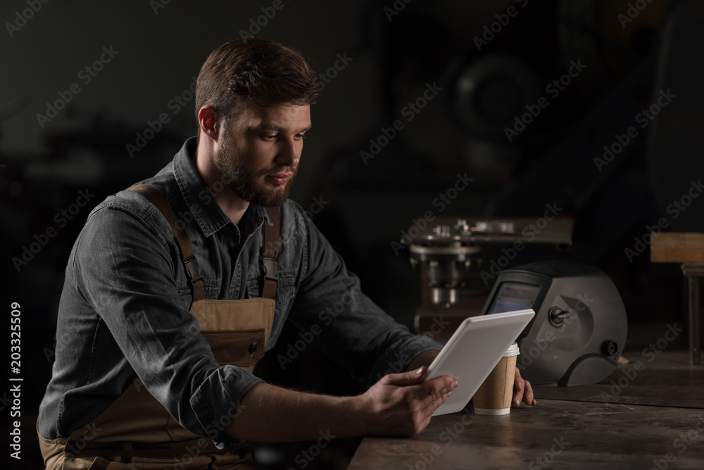 young male workman with paper cup of coffee using digital tablet young male workman with paper cup of coffee using digital tablet