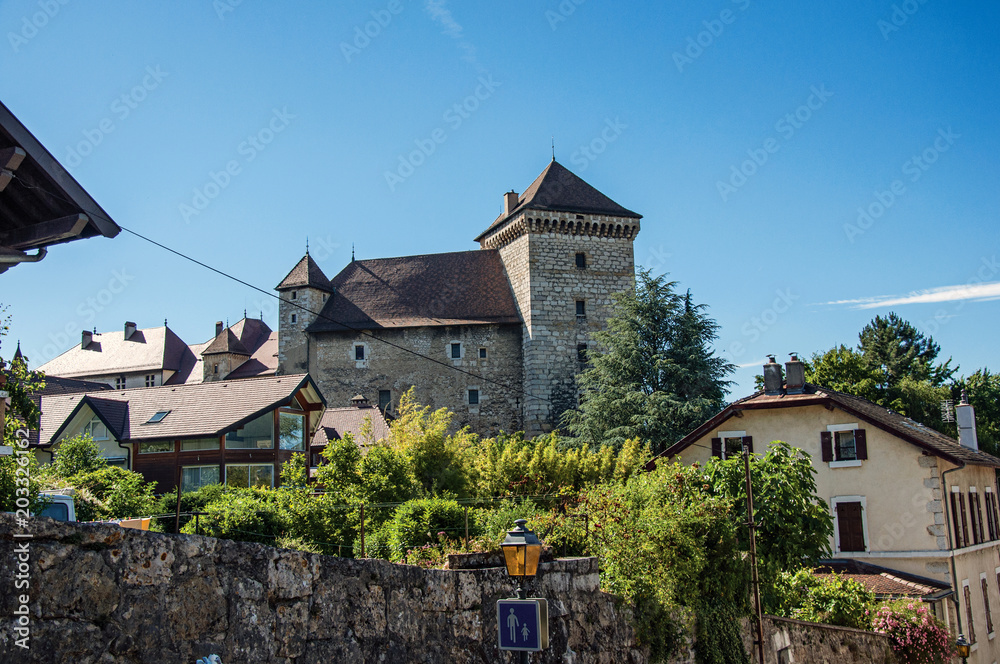 Partial view of Annecy castle and houses with a wall in foreground and blue sky, city center of Annecy. Located in the department of Haute-Savoie, Auvergne-Rhone-Alpes region, southeastern France.