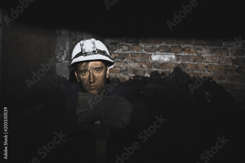 a miner with a pick sitting on the corner all tired and dirty from the coal dust after a hard work in the mine