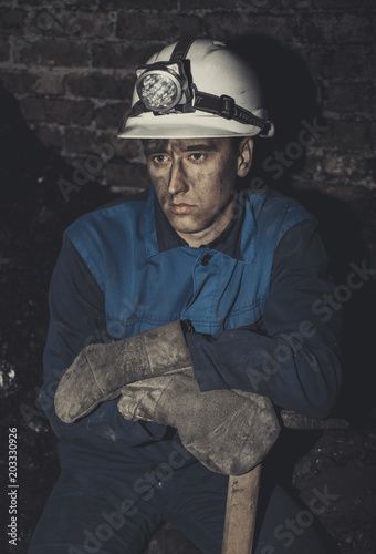 a miner with a pick sitting on the corner all tired and dirty from the coal dust after a hard work in the mine