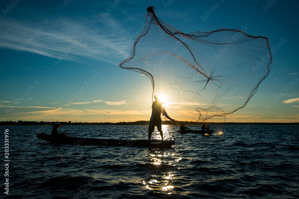 Naklejka premium Niezidentyfikowana sylwetka człowieka rybaka na łodzi łowiącej za pomocą sieci rybackiej