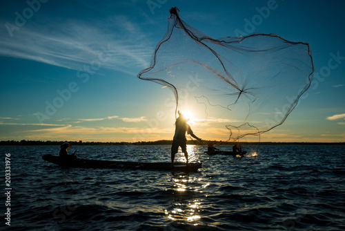 Fototapeta Un-identified silhouette fisher man on boat fishing by throwing fishing net